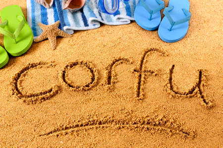 The word Corfu written on a sandy beach, with beach towel, starfish and flip flops.の写真素材