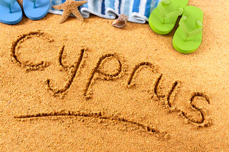 The word Cyprus written on a sandy beach, with beach towel, starfish and flip flops.の写真素材