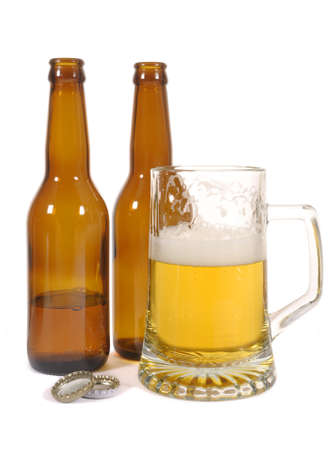 Half empty glass of beer with brown bottles against a white backgroundの写真素材