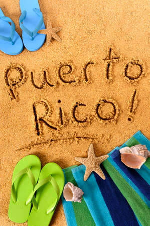 The words Puerto Rico written on a sandy beach, with beach towel, starfish and flip flops.の写真素材