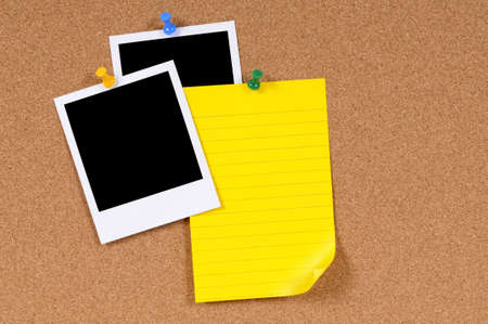 Blank photo prints with yellow writing paper pinned to a cork bulletin board.の写真素材