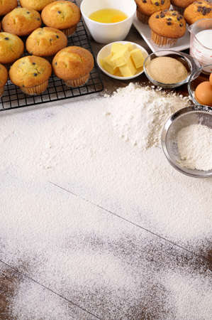 Baking background with dusted flour on a dark wood table with freshly baked muffins and ingredients.の写真素材
