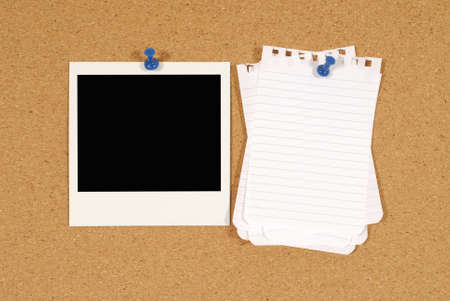 Cork notice or bulletin board with blank instant camera photo print and several sheets of untidy torn notepaper.の写真素材