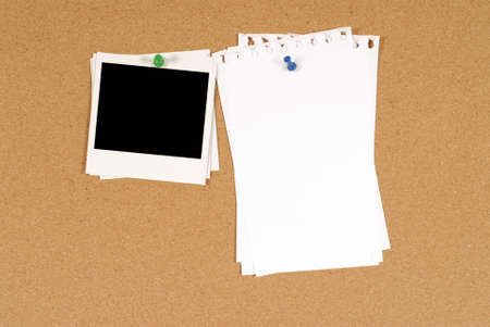Cork notice or bulletin board with a stack of blank instant camera photo prints and several sheets...