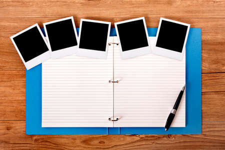 Photo album on a wood table with several blank instant camera photo prints.  Space for copy.の写真素材