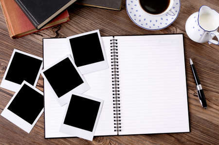 Photo album on a wood table with several blank instant camera photo prints, coffee and books.  Space for copy.の写真素材