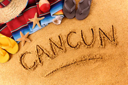 The word Cancun written in sand on a Mexican beach, with sombrero, straw hat, traditional serape blanket, starfish and maracas.の写真素材