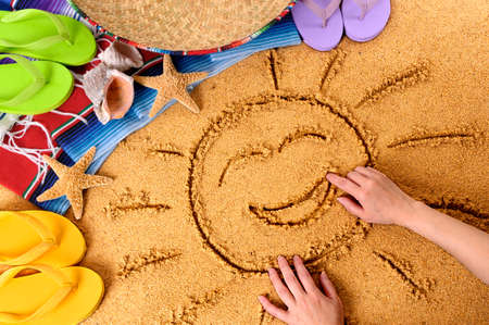 Child drawing a smiling sun in sand on a Mexican beach, with sombrero, straw hat, traditional serape blanket, starfish and seashells.の写真素材