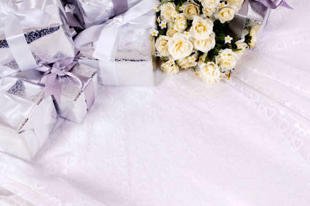 Wedding gifts background with white rose bouquet laid on bridal lace.  Space for copy.の写真素材