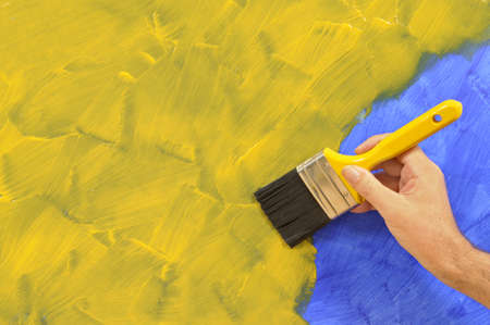 Man holding a paintbrush with a partly finished blank blue and yellow painted wall.  Space for copy.の写真素材