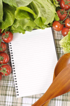 Selection of salad vegetables with blank recipe book or shopping list and wooden serving spoons.の写真素材