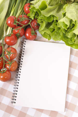 Selection of salad vegetables with blank recipe book or shopping list on a check tablecloth.の写真素材