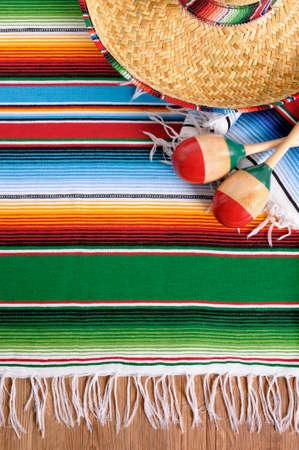 Mexican background with sombrero straw hat, maracas and traditional serape blanket or rug on a wood floor.  Space for copy.の写真素材