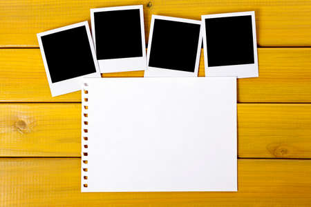 Four blank photo prints on a wood desk or table with a page torn from a spiral notebook.  Space for...