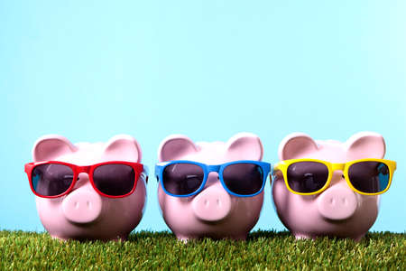 Three pink piggy banks with sunglasses on grass with blue sky Three pink piggy banks with sunglasses on grass with blue sky
