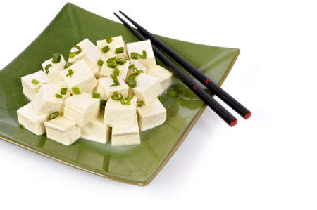 Cubes of fresh tofu garnished with spring onion slices on a green plate with white background.の写真素材