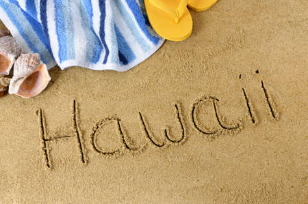 The word Hawaii written in sand with flip flops and beach towelの写真素材