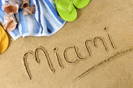 The word Miami written in sand with flip flops and beach towel.の写真素材