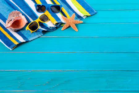 Beach scene with striped towel, sunglasses, starfish and seashell on old weathered blue painted wood decking.  Space for copy.の写真素材