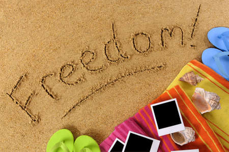 Beach background with towel, flip flops, blank photos and the word Freedom written in sandの写真素材