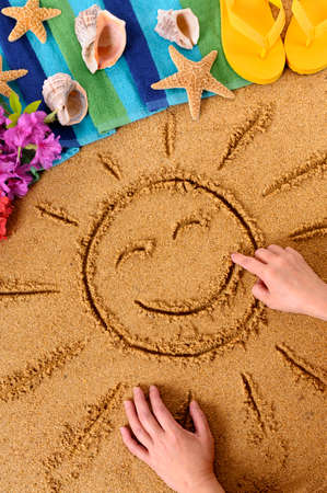Child drawing a smiling sun on an Hawaiian beach, with traditional flowers, beach towel, starfish and flip flopsの写真素材