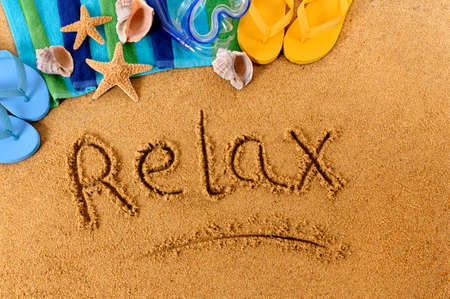 The word Relax written on a sandy beach, with scuba mask, beach towel, starfish and flip flopsの写真素材