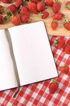 Strawberries with blank recipe book on a chopping board and red check tablecloth.の写真素材