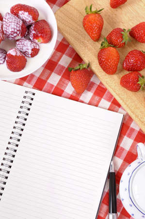 Strawberries and cream with blank recipe book on a chopping board and red check tablecloth.の写真素材