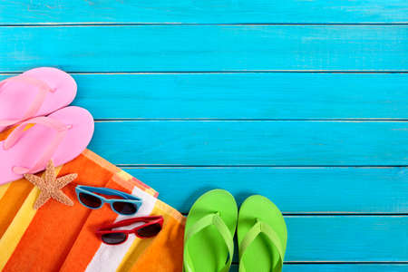 Beach scene with orange striped towel, pairs of sunglasses and flip flops on old blue painted wood decking.  Space for copy.の写真素材