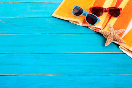 Beach scene with orange striped towel, starfish and sunglasses on old blue painted wood decking.  Sharp focus on the sunglasses.  Space for copy.の写真素材