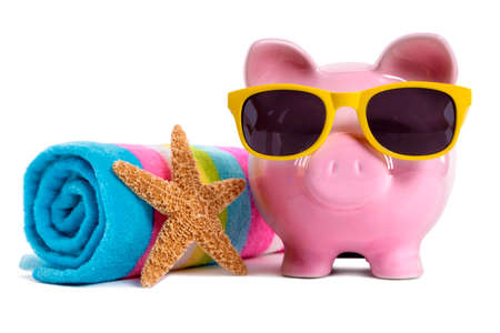 Pink piggy bank wearing yellow sunglasses on a beach with starfish and beach towel.  Isolated on white.の写真素材