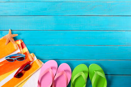 Beach background scene with orange striped towel, sunglasses, starfish and flip flops on old blue painted wood decking.  Space for copy.の写真素材