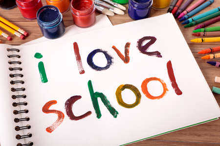 The words I Love School painted on a white art book with various paints, crayons and pencils on a school desk.の写真素材