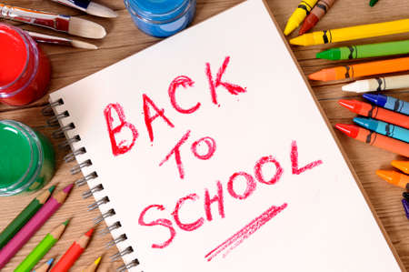 The words Back to School written on a white notebook with various paints, crayons and pencils on a school desk.の写真素材