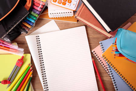 Busy student's desk with open notebook, school bag, text books and various pencils and crayons.の写真素材