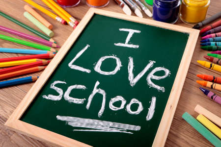 The words I Love School written on a small elementary blackboard with various paints, crayons and pencils on a school desk.の写真素材