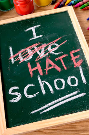 The words I Hate School written on a small elementary blackboard with various paints, crayons and pencils on a school desk.の写真素材