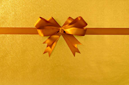 Gold gift bow and ribbon, shiny metallic foil paper background, straight horizontal