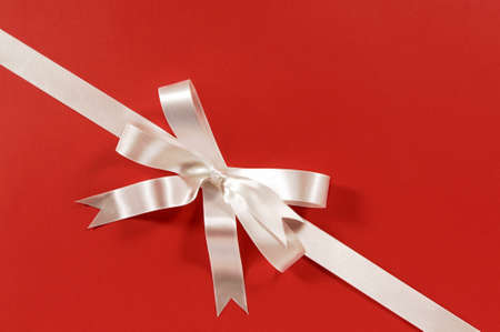 Diagonal gift ribbon and bow in white satin on red paper backgroundの写真素材