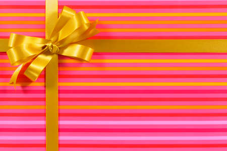 Gift border frame with gold ribbon bow and pink candy stripe background paperの写真素材