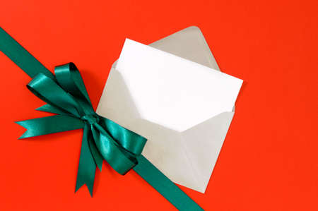 Christmas or birthday card on red gift paper background with green ribbon bow.の写真素材