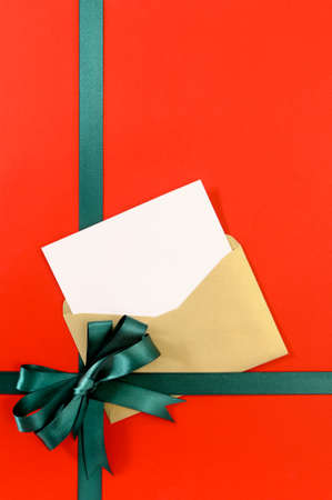 Open Christmas or birthday card with green gift ribbon bow on plain red background paper, copy space, verticalの写真素材