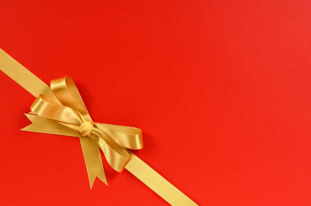 Gold gift bow ribbon corner diagonal isolated on red wrapping paper backgroundの写真素材