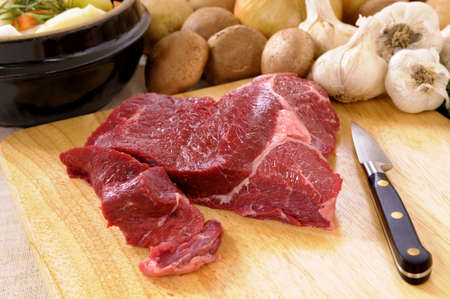Preparing beef for casserole or stew with ingredients and knife on kitchen chopping board.の写真素材
