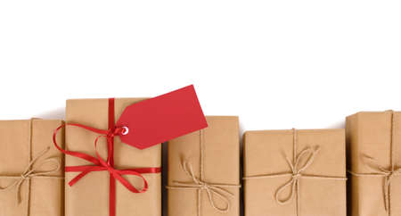 Border of brown paper parcels, one unique with red ribbon bow and gift tag or label, isolated on white backgroundの写真素材