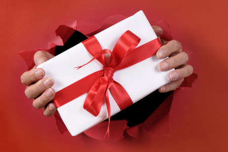 White gift with ribbon being delivered through a red torn paper background.の写真素材