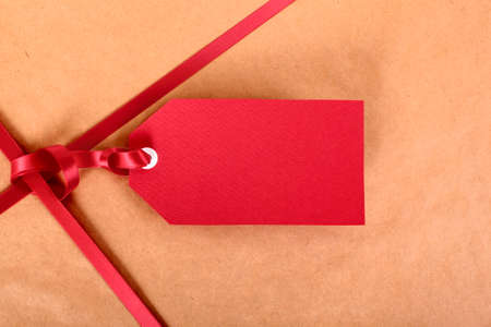 Closeup red gift tag and ribbon, brown parcel wrapping paper background, copy space.の写真素材
