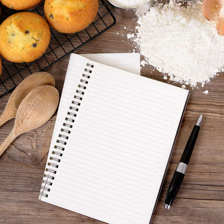 Blank cookbook or writing book on a dark wood table with freshly baked muffins and ingredients.の写真素材