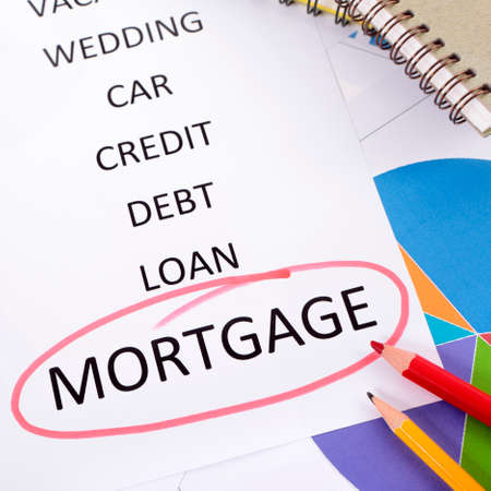 The word Mortgage circled in red with a list of saving and debt obligations surrounded by graphs, charts, books and pencils.の写真素材