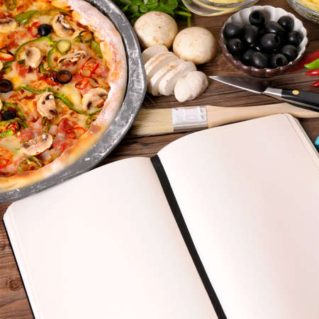 Freshly baked Pizza with blank notebook or cookbook surrounded by various ingredients.の写真素材